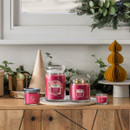 A festive display of Yankee Candles in different sizes and styles, all in the “Santa on Skis” fragrance. They are arranged on a wooden sideboard decorated with greenery, wrapped presents, and seasonal ornaments.