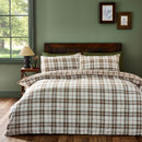 A stylish bedroom featuring a duvet cover and pillowcases with a white base and a bold plaid pattern in burnt orange, brown, and sage green, styled with plain olive green pillow shams and a wooden headboard.