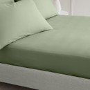 A view of a green fitted sheet on a bed next to matching pillows