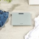 Digital bathroom scale on beige tiles, flanked by folded jeans on the left and a white towel on the right, conveying a sense of daily routine.