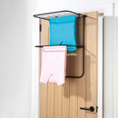 A black over-the-door drying rack holds a blue and a pink garment, mounted on a wooden door with a black handle. Bright, minimalistic setting.