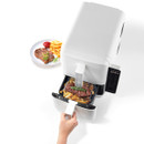 A hand pulls out an air fryer drawer containing steak and fries garnished with rosemary; a plated meal with ketchup is placed beside it.