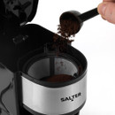 Close-up of coffee grounds being poured into a metal coffee machine filter. The machine is branded "Salter" and has a sleek, modern design.