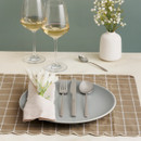 Elegant table setting with a grey plate on a brown checkered placemat. Cutlery, a white napkin with flowers, two wine glasses, a spoon, and a vase complete the arrangement.