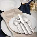Elegant dining setup with polished silver cutlery—knife, fork, and spoons—placed on white plates atop a beige napkin. A glass bottle and blue fabric add a sophisticated touch.
