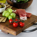 Fresh grapes, tomatoes, prosciutto slices, and olives arranged on a rustic serving board.