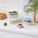 Stacked LocknLock rectangular food storage containers filled with fresh spinach, cashews, grapes, and blueberries on a white kitchen counter.