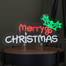 Illuminated Merry Christmas LED neon sign displayed on a tabletop, featuring red and white lettering with a green holly leaf design, ideal for festive indoor Christmas décor.