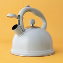 Light blue stovetop kettle with ergonomic handle and flip-top spout cover against a mustard yellow background.