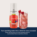 Bottle of SodaStream Red Berries mix alongside a glass of sparkling red berry drink with ice and fresh berries.