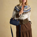 Woman holding a navy mini grab bag with leather handles and adjustable crossbody strap against a beige background.