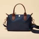 Front view of a navy mini grab bag with brown leather handles, gold zip fastening, and detachable strap.