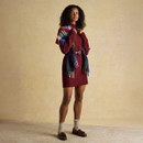 Woman in a burgundy knitted dress styled with a multicoloured check scarf draped across shoulders, belted at the waist.