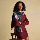 Woman styled in a burgundy knit dress with a multicoloured check scarf featuring fringe ends.
