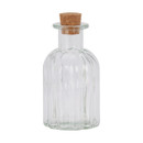 A clear, ribbed glass bottle with a bulbous shape and a cork stopper. The bottle is empty, standing upright against a plain white background.