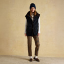 Full outfit with woman wearing navy knit beanie, black gilet, striped trousers, and loafers.