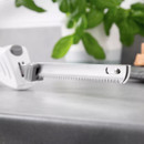 A sharp electric knife rests on a grey worktop with fresh green leaves in the background, creating a clean and modern kitchen atmosphere.