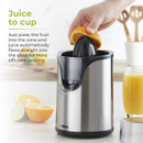 A hand squeezes an orange on a sleek silver juicer, with fresh juice flowing into a glass. Text promotes easy use. Bright, inviting kitchen scene.