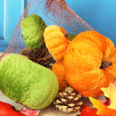 Close-up of orange and green decorative pumpkins, gourds and pine cones contained in a brown mesh bag.