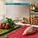 Joseph Joseph Folio Icon chopping board set in use with fresh vegetables, bread, and chicken on colour-coded boards.