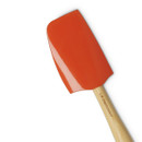 Close-up of the Le Creuset Volcanic Spatula head, showing its glossy silicone finish and part of the wooden handle engraved with the Le Creuset logo.