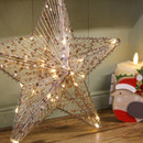 Close-up of a light-up Christmas star decoration with shimmering silver threads, gold sequins and warm white fairy lights, displayed beside a festive robin candle holder.