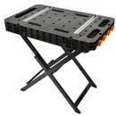 Foldable black workbench with a perforated tabletop, sturdy metal legs, and orange clamps. Designed for versatile, portable use in various tasks.