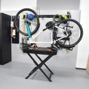 Bicycle mounted upside down on a black stand in a garage. Tools and sports gear hang on wall racks. The setting is organized and neat.