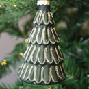 A close-up of a green glass Christmas tree decoration featuring tiered branches outlined in gold glitter, hanging from a Christmas tree surrounded by festive lights.