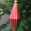 A close up view of a red glass Christmas decoration with a ridged, elongated teardrop shape, detailed with gold glitter.
