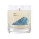 Sea Breeze candle burning in a transparent glass jar with minimalist label showing a crashing blue wave, symbolising a cool and invigorating marine fragrance.