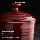 Close-up of a shiny red ceramic pot lid with a handle against a black background. Text reads "BARBARY & OAK" and "Dishwasher Safe, For convenience in the home."