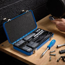 The Draper 45-piece socket set open on a wooden workbench next to bolts and tools. A person is using one of the ratchets, and the blue metal case with its fitted interior is clearly visible.