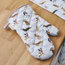 A light blue quilted oven glove decorated with assorted dog illustrations, resting on a wooden kitchen countertop.