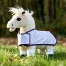 A plush toy horse stands on grass, wearing a patterned purple blanket. The background shows a blurry, wooded area, creating a cheerful, outdoor vibe.