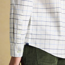 Close-up of a person wearing a white Joules shirt with a blue and black grid pattern, paired with dark green corduroy pants. The scene conveys a casual, classic style.