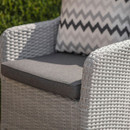 Close-up of a grey wicker armchair with a dark grey seat cushion and a patterned cushion resting against the back.