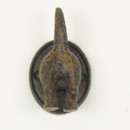 A rustic, antique bronze hook shaped like the rear of a dog with its tail up, mounted on an oval base, conveying a humorous tone.