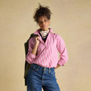 A woman wearing a pink and white striped shirt styled with rolled sleeves, a scarf and a jacket draped over her shoulder.