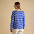 Back view of a woman wearing a blue and light blue striped long-sleeve top with a relaxed fit, shown against a soft beige backdrop.