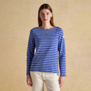 Woman wearing a blue and light blue striped long-sleeve top with a boat neckline, paired with cream trousers, standing against a neutral background.