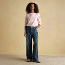 Woman wearing a pink and white striped Breton top paired with wide-leg blue jeans and casual boots against a neutral backdrop.