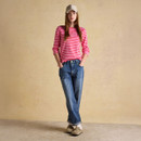 A woman standing wearing a pink and red striped Breton top paired with relaxed blue jeans and a beige baseball cap.