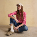 A woman sitting on the floor wearing a pink and red striped long-sleeve Breton top with blue jeans and a beige cap.
