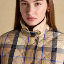 A woman wearing the beige checked quilted jacket with the high collar fastened, highlighting the gold poppers and structured neckline.
