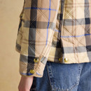 Detail of the sleeve and side of a beige and brown check quilted jacket, showing gold popper cuffs and diamond stitching.