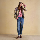 Woman wearing a beige and brown check quilted jacket layered over a pink cardigan, styled with relaxed blue jeans, white socks, and brown leather shoes.