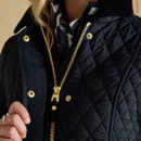 Close-up of the gold zip and popper fastening on a black quilted jacket, showing the textured quilted exterior.