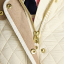 Detail of a cream quilted jacket zip and gold hardware, highlighting the textured corduroy trim.