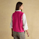 Back view of a bright pink sleeveless knitted vest, worn over a white ruffled blouse with checked trousers.